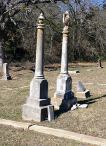 These tall columns stand out in a cemetery. The one on the right has a draped urn carving on top.