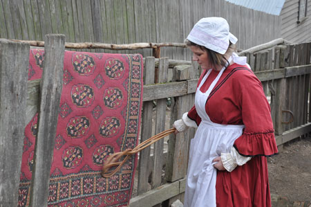 Beating a rug in the mid 1850s.  The object in her hand was known as a “carpet beater” and took a fairly strong girl to rid the rug of the accumulation of dirt from the winter.  (Sovereign Hill Education Blog, servant-carpet-beating.)